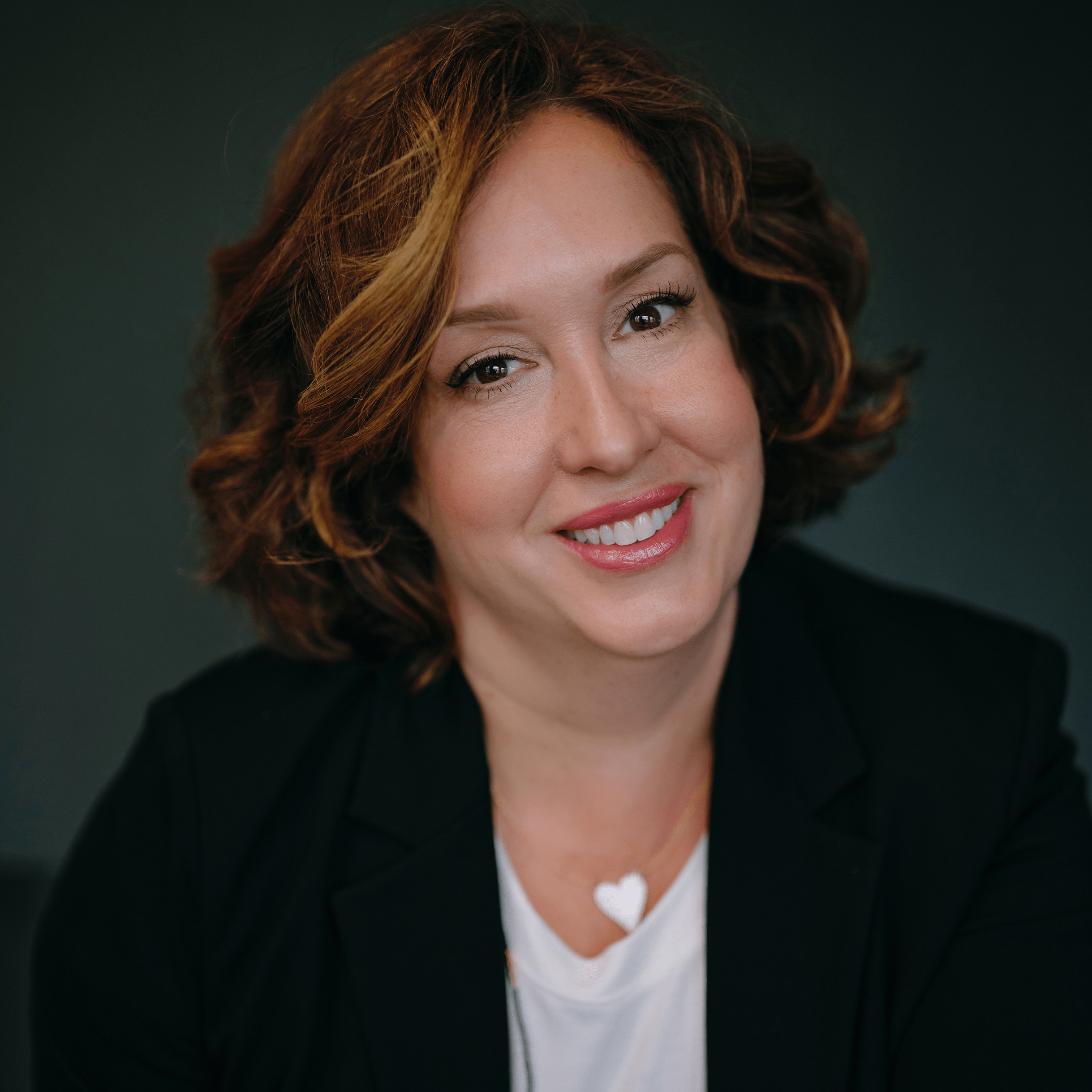 Dr. Julie smiles warmly at the camera in a professional headshot, dressed in attire that reflects her commitment to inclusion. The greenish background symbolizes growth and a welcoming environment, highlighting her dedication to creating inclusive spaces