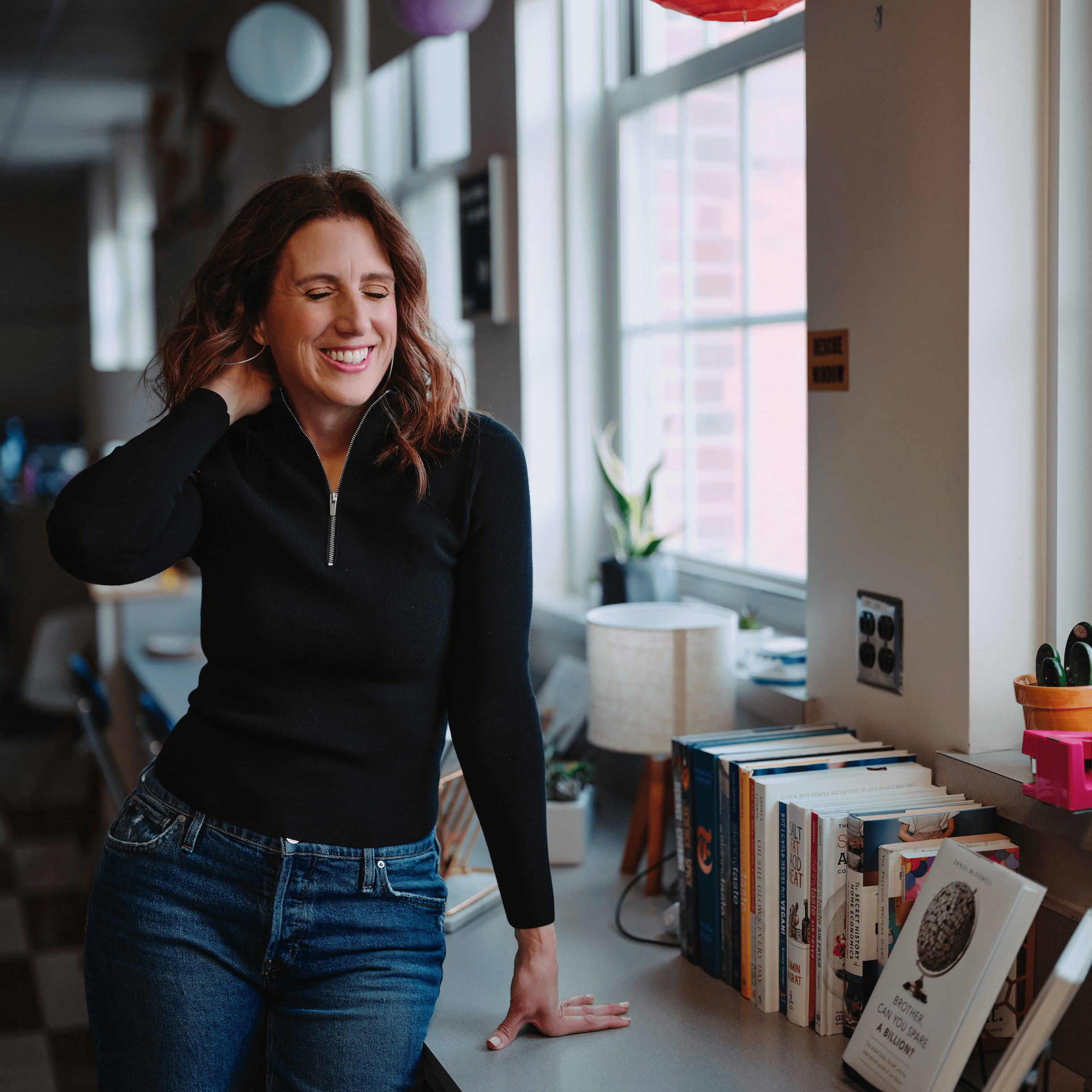 Dr. Kristie is caught mid-pose, smiling thoughtfully as she adjusts her hair with one hand. Her book, 'The Way to Inclusion,' rests on the desk beside her, symbolizing her dedication to promoting inclusive practices in education.